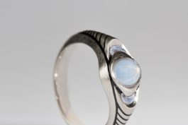 Mondenkind, Detailbild: Ein Ring im kühlen Mondglanz gefertigt in Weißgold mit dem Schimmer des Mondsteins und schwarzen Emaillelinien.